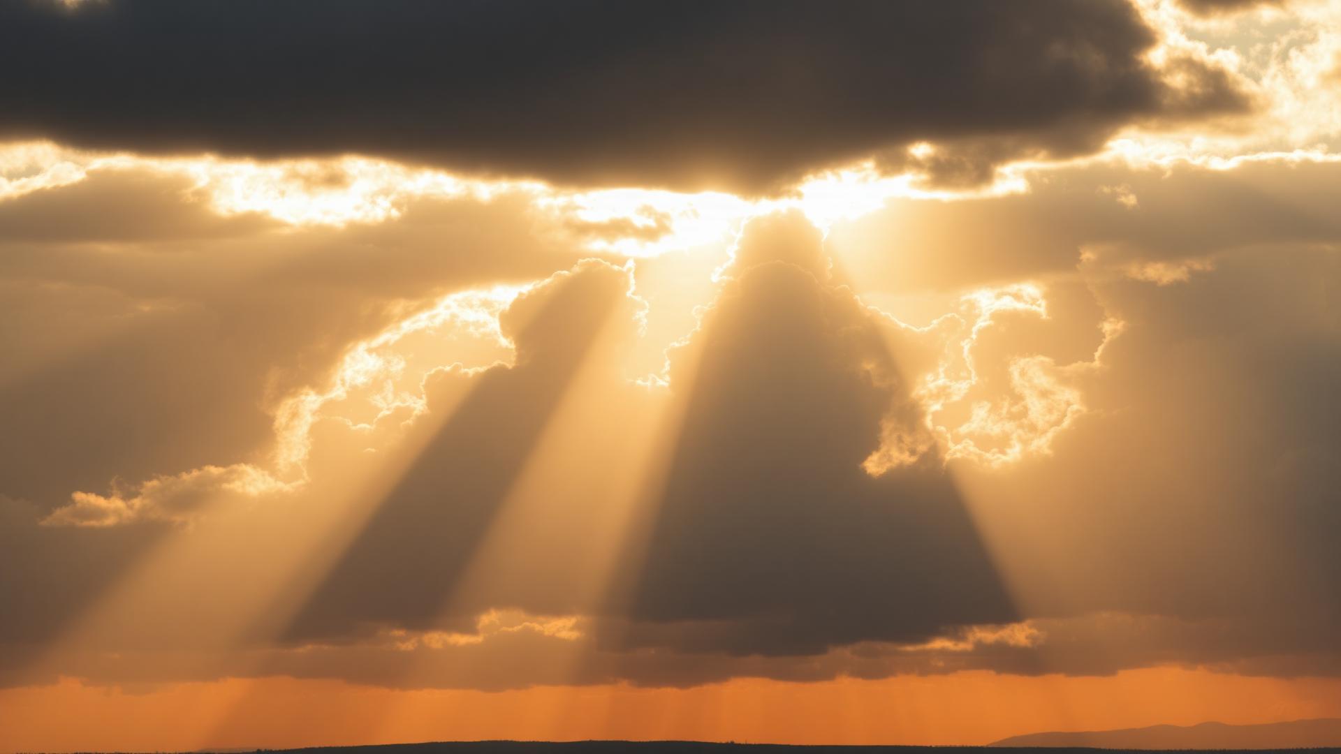 Golden sunlight breaking through dark clouds over a vast horizon
